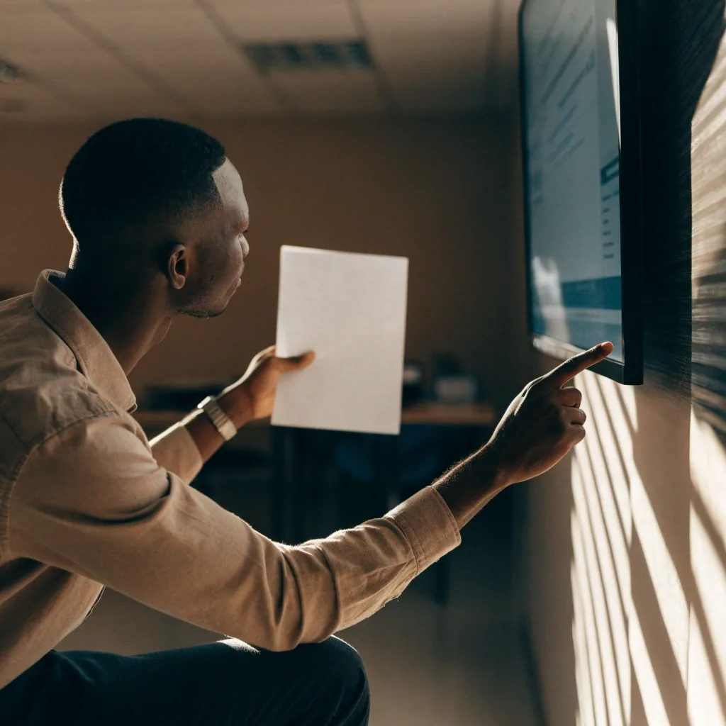 Over-the-shoulder view of a designer reviewing a printed layout at a sunlit desk